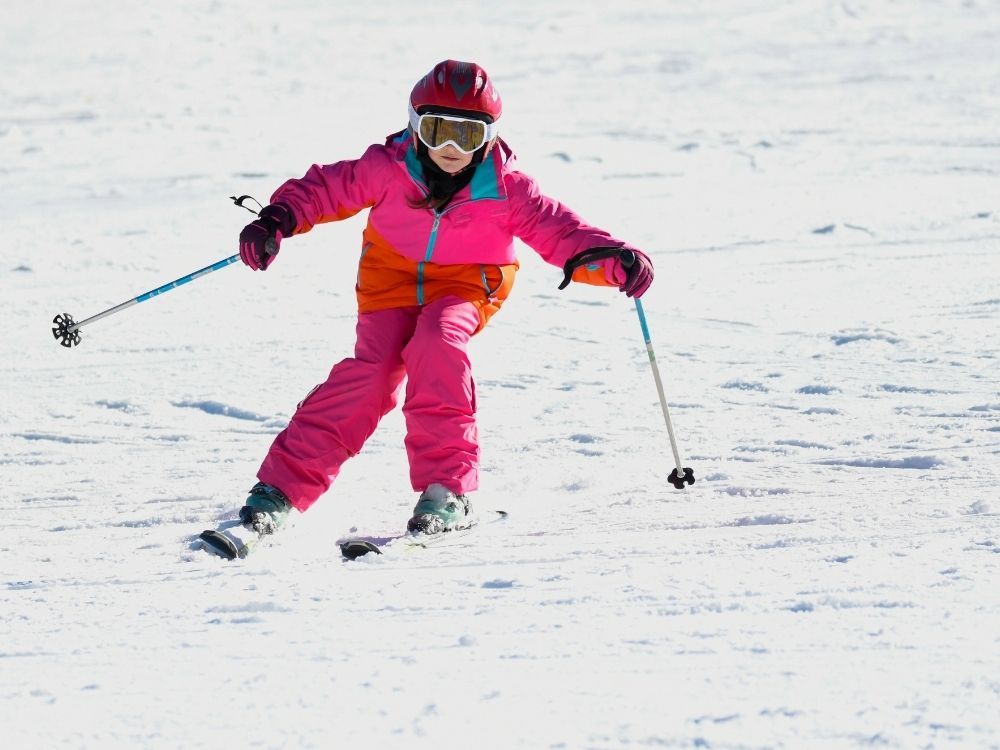 skivakantie meisje in roze skipak op ski's